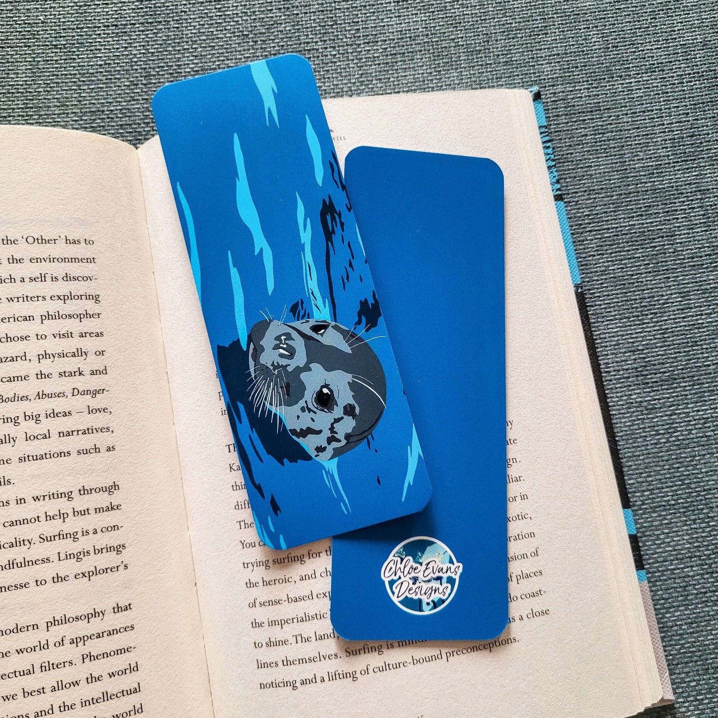 Illustrated grey seal bookmark showing a seal swimming through water, printed on tear-proof paper – design by Chloe Evans