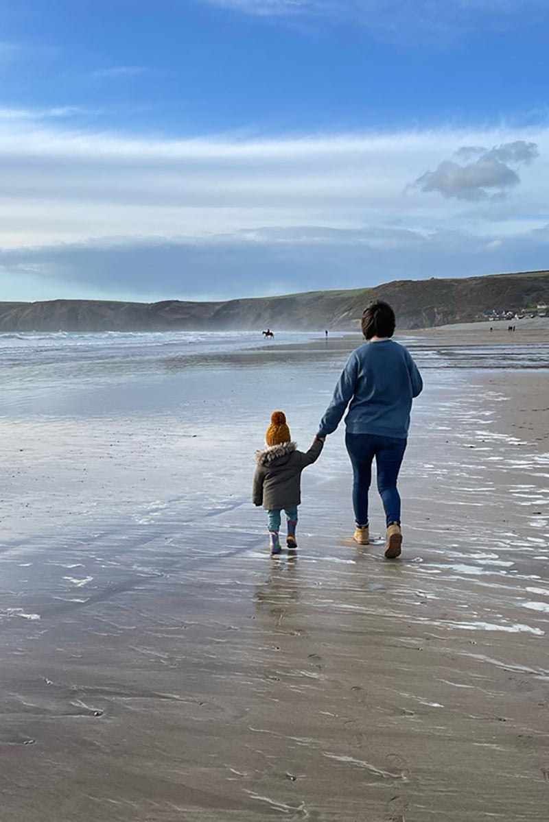 A photo of Chloe and her son walking on Newgale beach in Pembrokeshire.