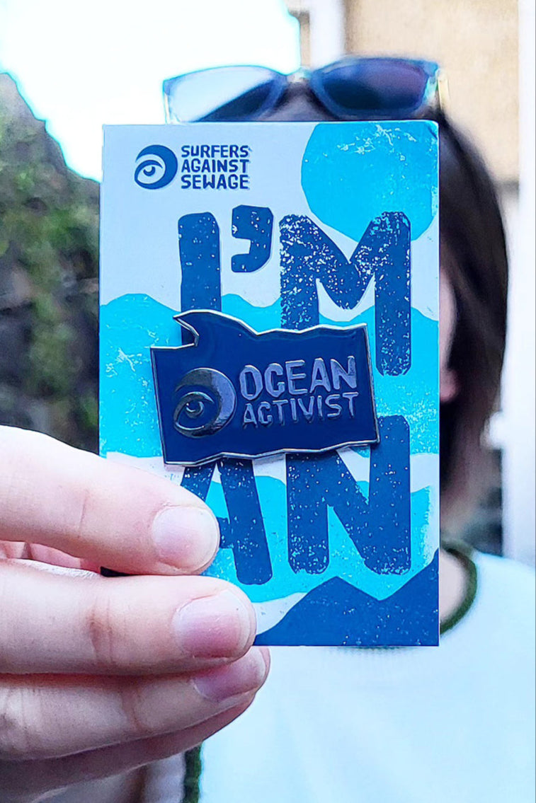 A photo of someone holding a Surfers Against Sewage "Ocean Activsist" pin badge up close to the camera.