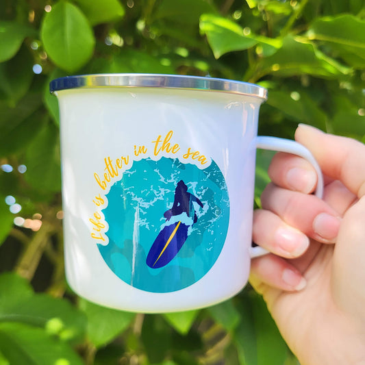 Hand-illustrated enamel mug with peaceful female surfer sitting on board photographed outside in natural light