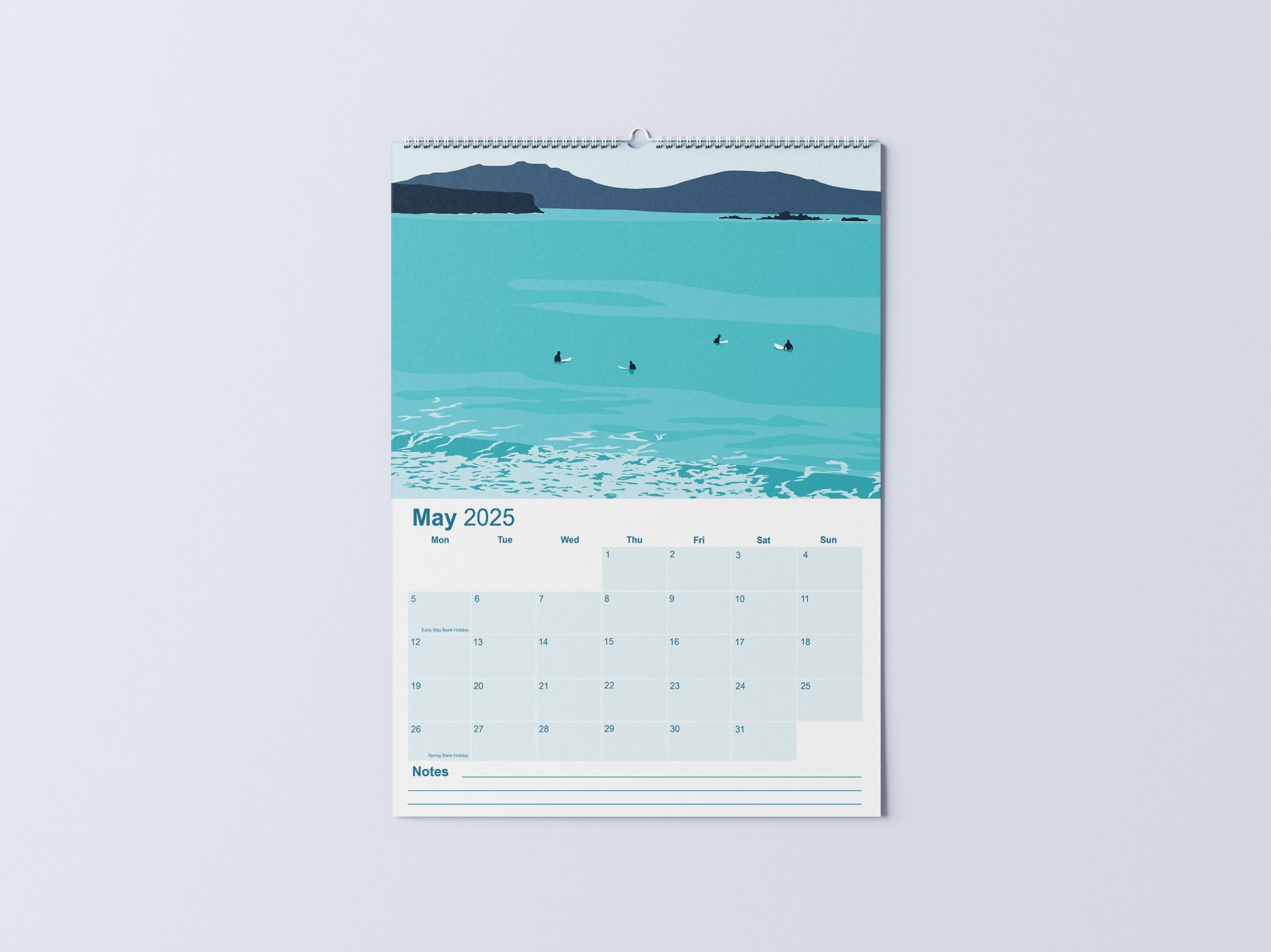 Digital mockup of an A3 coastal wall calendar, showing the May page with an illustration of surfers sat on their boards in the sea.