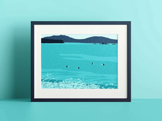 A blue print of surfers sat on the surfboards with an island in the distance, in a navy frame on a blue wall