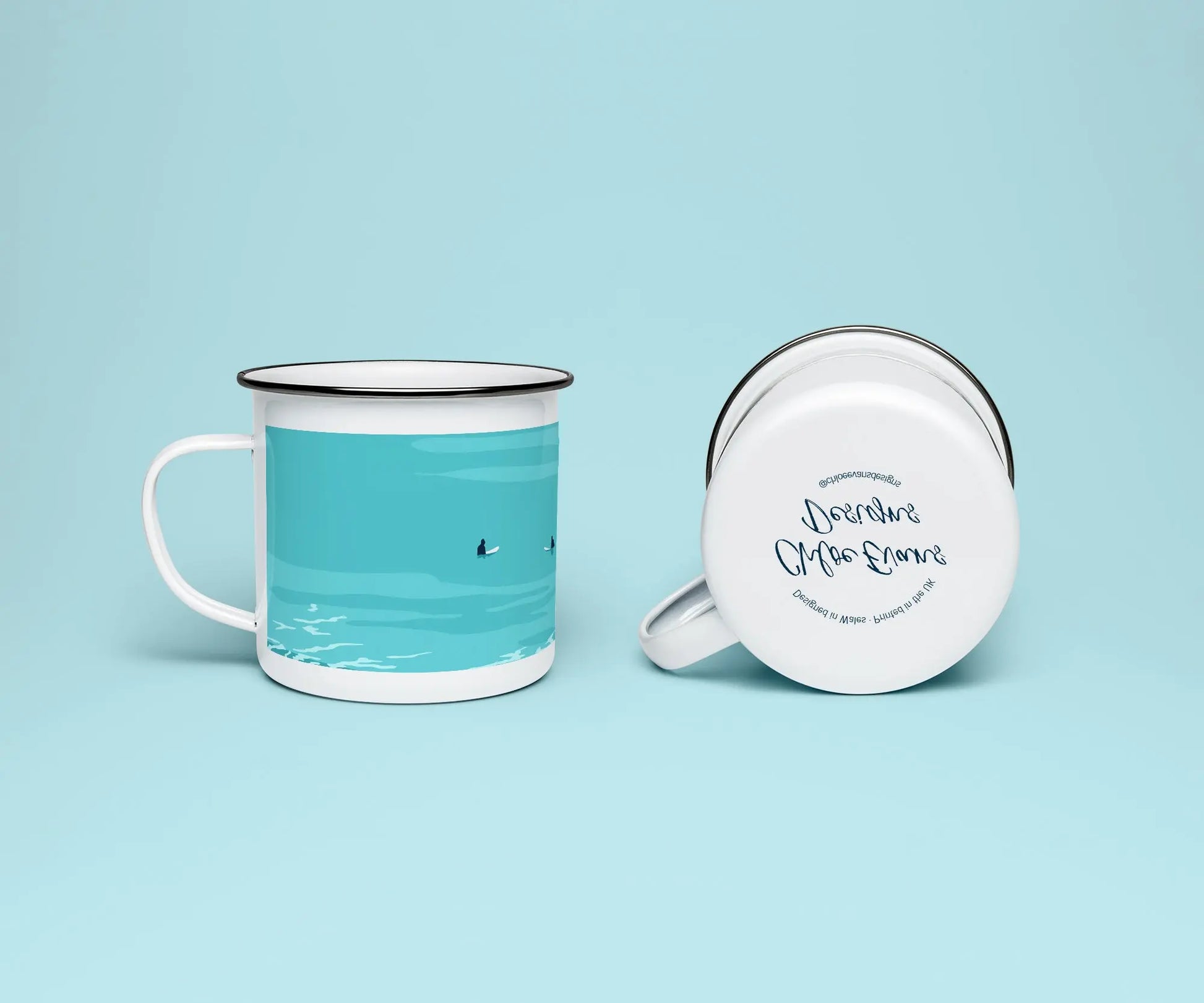 A white enamel mug from two perspectives: one of the mug on its side showing the branded base stamp on the bottom of the mug, and the other of the mug upright showing the blue print of two surfers; all on a light blue background.