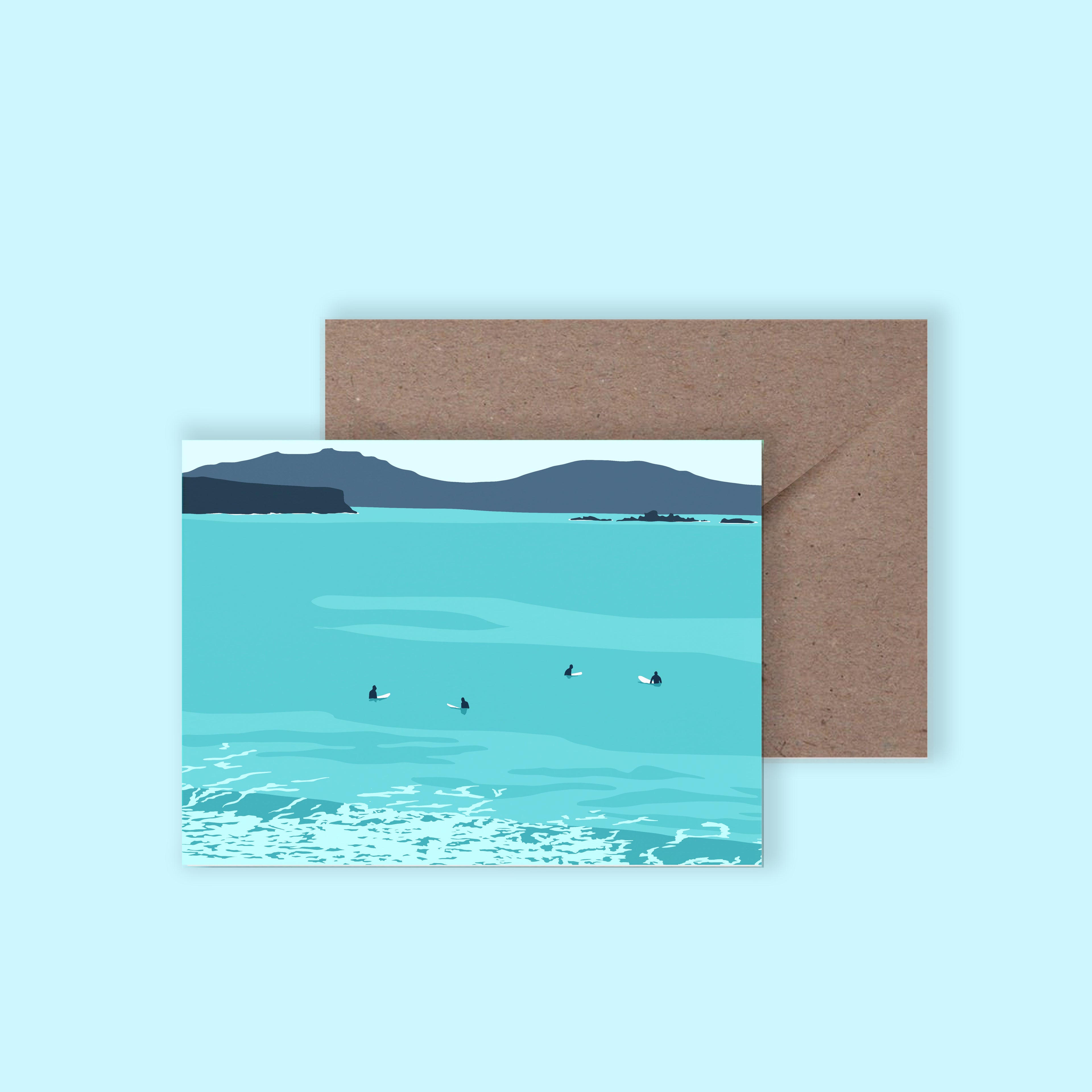 A mockup of a greeting card with an illustration of surfers sat on their surfboards, with a brown envelope behind on a light blue background.