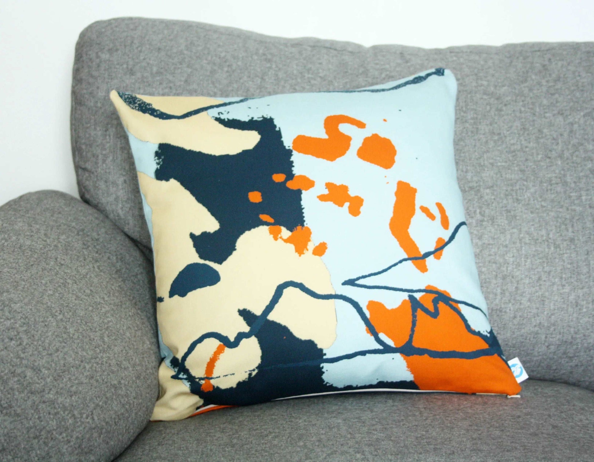 Handmade blue and orange abstract coastal cushion on grey sofa.