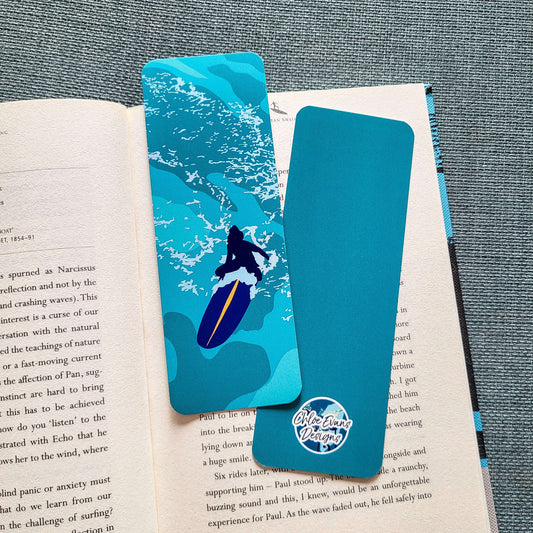 Bookmark featuring a woman sitting on a surfboard in calm water – “Serenity” design by Chloe Evans