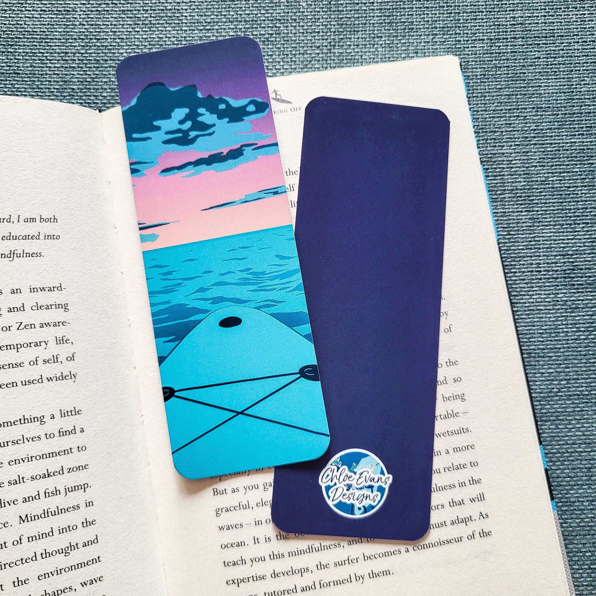 Bookmark showing the nose of a paddleboard on water at sunset with pink and purple sky – “Sunset SUP” design by Chloe Evans