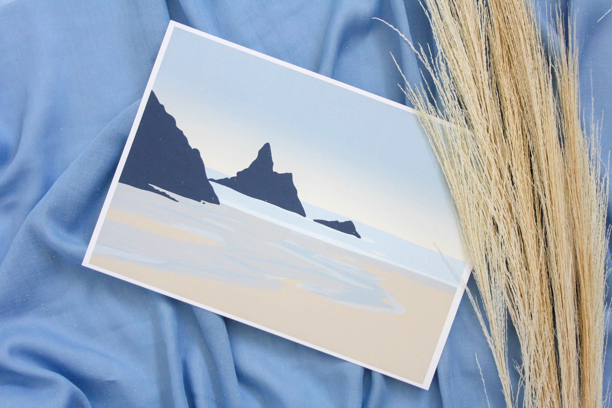 Photo of blue and beige Broad Haven South beach print on blue backdrop with pampas grass prop.