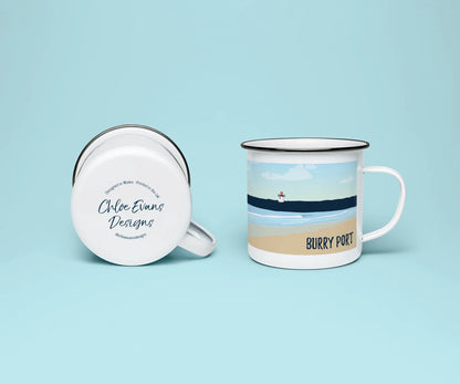 A white enamel mug from two perspectives: one of the mug on its side showing the branded base stamp on the bottom of the mug, and the other of the mug upright showing the blue print of Burry Port beach and lighthouse; all on a light blue background.