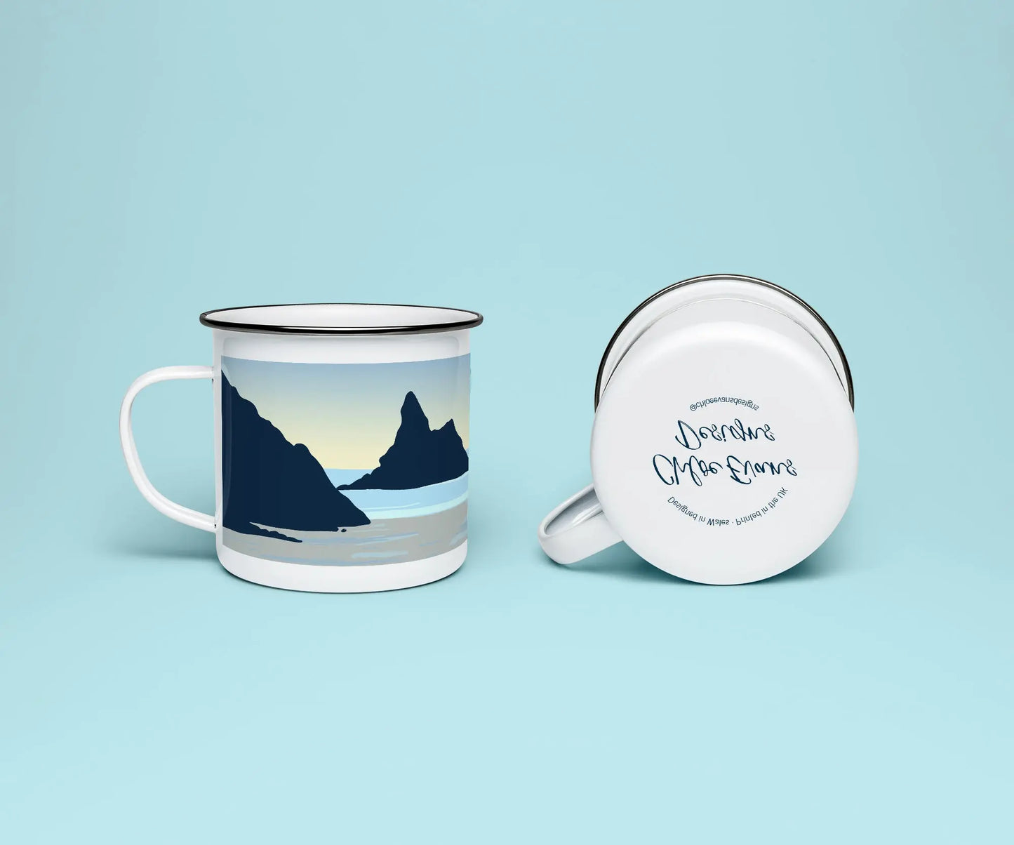 A mock up of a white enamel mug from two perspectives; one of the mug on its side looking at the bottom of the mug and the branded base stamp, and the other of the mug upright showing the print of an orange and blue beach scene, showing Church Rock and Broad Haven South, all on a light blue background.