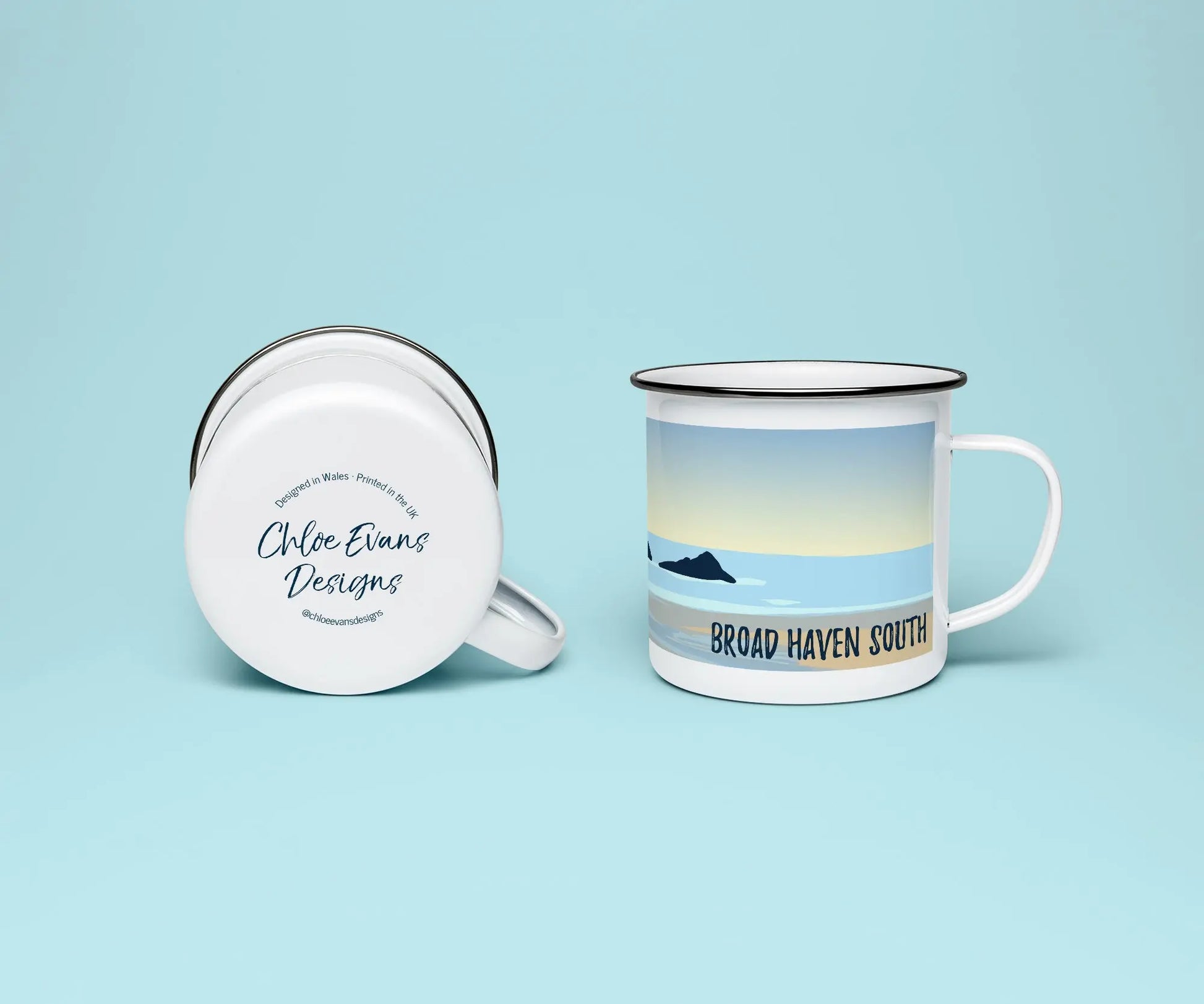 A mock up of a white enamel mug from two perspectives; one of the mug on its side looking at the bottom of the mug and the branded base stamp, and the other of the mug upright showing the print of an orange and blue beach scene, showing Church Rock and Broad Haven South, all on a light blue background.