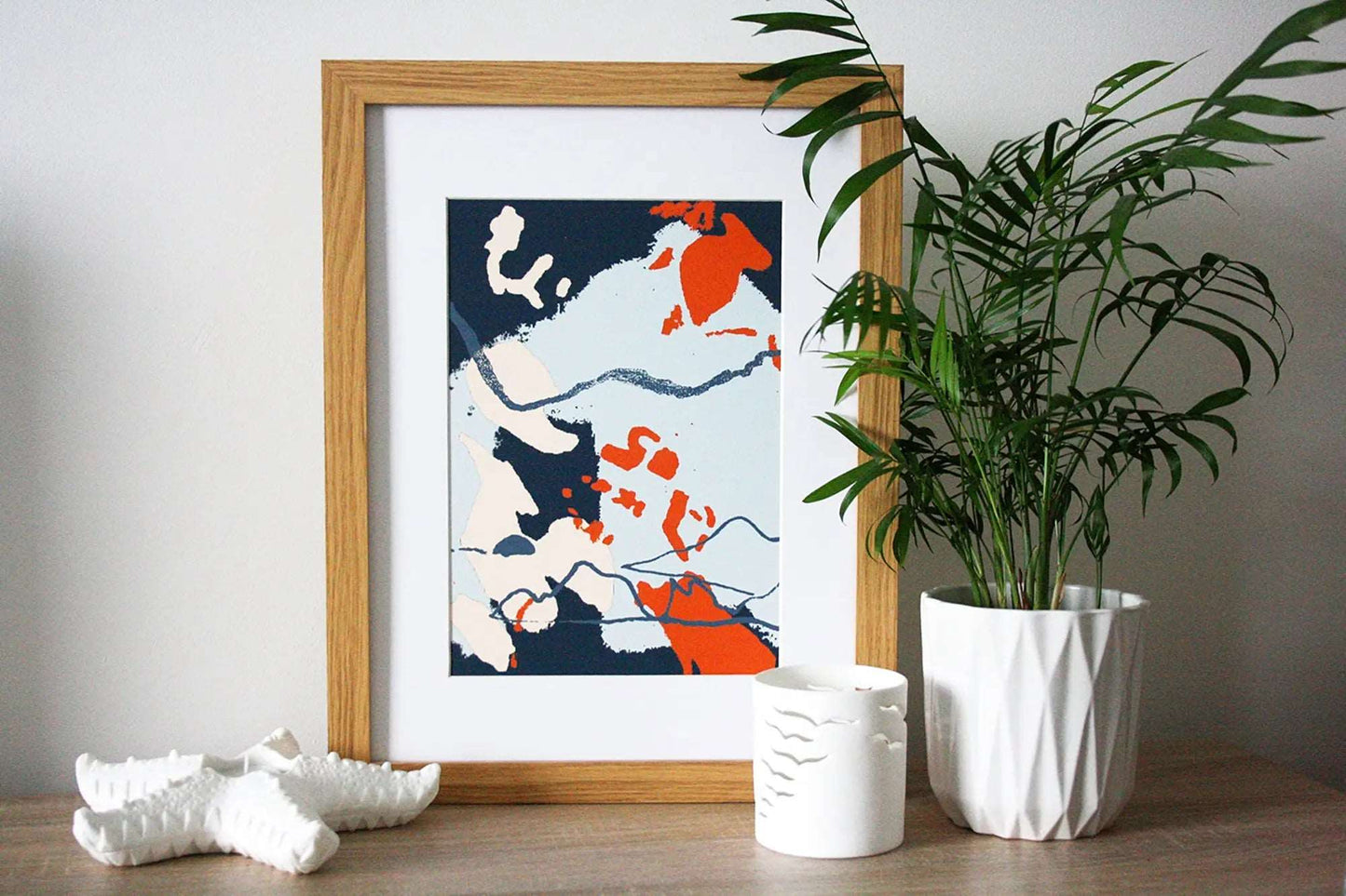 Photo of blue and orange Coastal Journey 9 abstract A4 print in wooden frame, surround by white home accessories and house plant