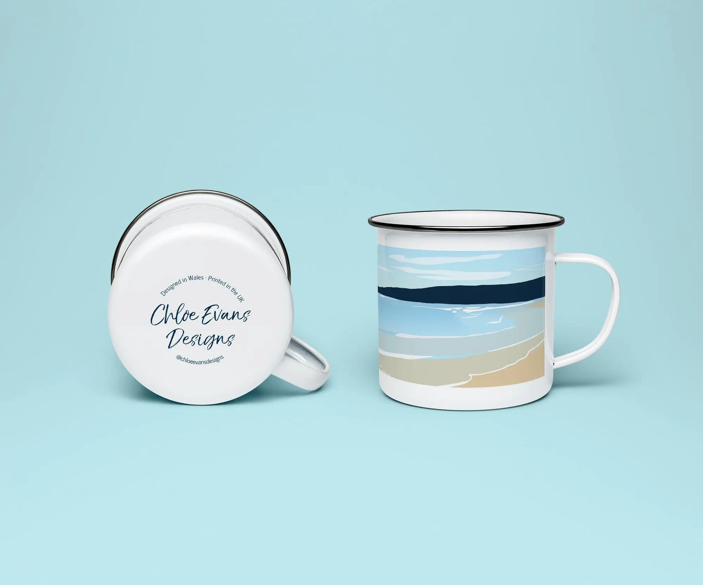 A mock up of a white enamel mug from two perspectives; one of the mug on its side looking at the bottom of the mug and the branded base stamp, and the other of the mug upright showing the print of Freshwater West beach, all on a light blue background.