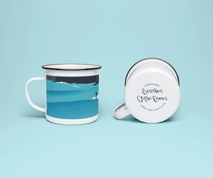 A white enamel mug from two viewpoints, one upright showing it's blue print of a surfer, and the other on it on its side showing the branded base stamp on the bottom of the mug; all on a light blue background.