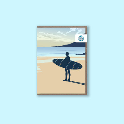 Christmas greeting card for surfers, with a surfer holding his surfboard wrapped in Christmas lights looking out to sea.