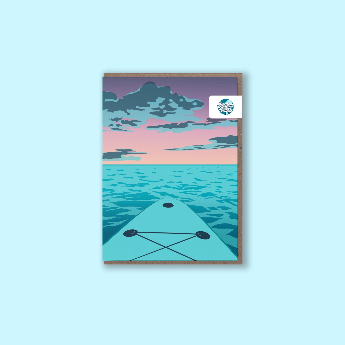 A mockup of a greeting card with an illustration of a purple sunset from the viewpoint of a paddle boarder on their board, with a brown envelope behind and a removable plastic-free packaging sticker, on a light blue background.