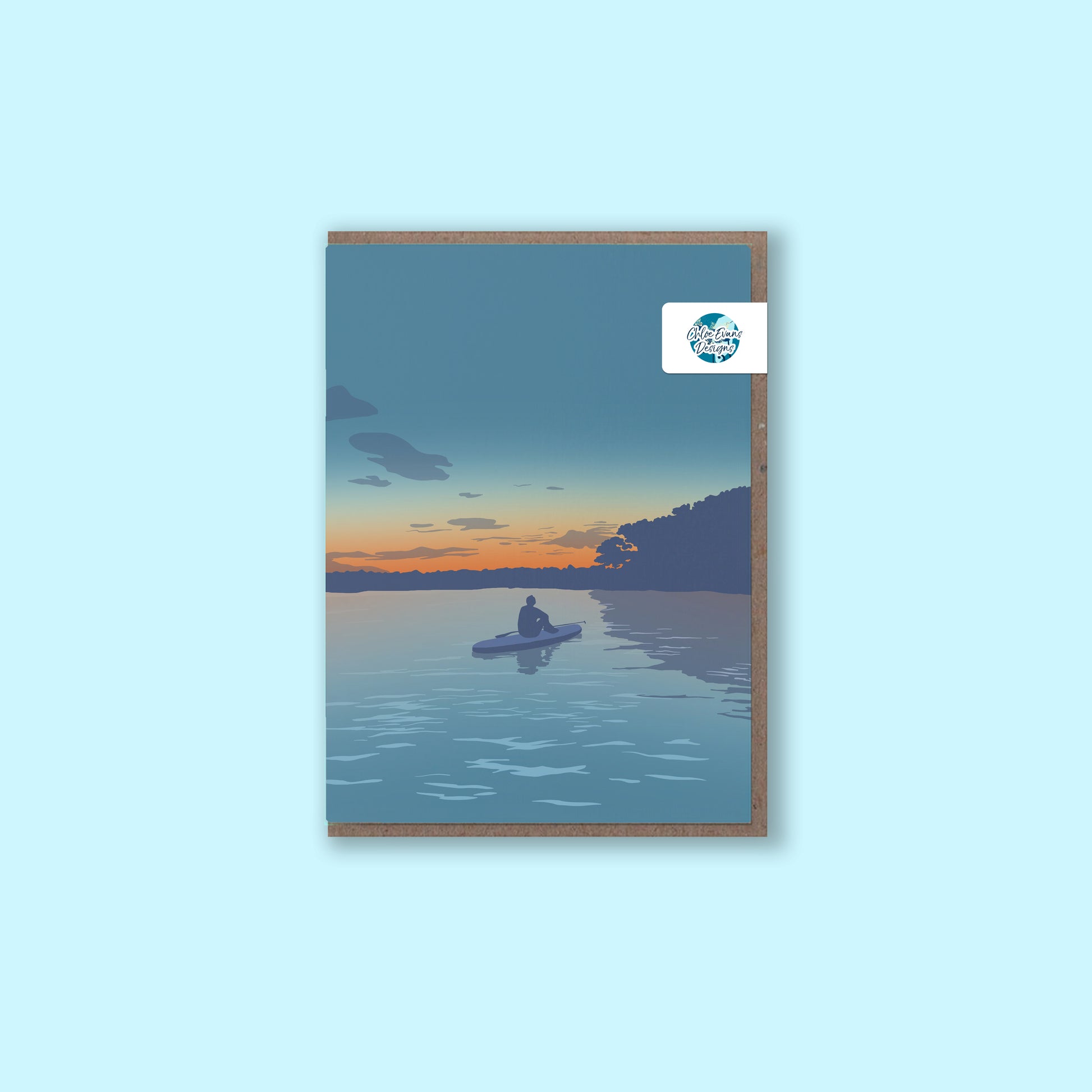 A mock up of a greeting card with an illustration of a paddleboarder sat on her board watching the sunset, with a brown envelope with a removable plastic-free packaging sticker on a light blue background.