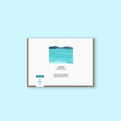 A mockup of the back of a greeting card showing the illustration of surfers sat on their surfboards that is on the front, with a brown envelope behind and a plastic-free removable packaging sticker, on a light blue background.