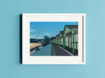 A print of the beach huts at Langland bay, Gower, in a white frame on a blue wall