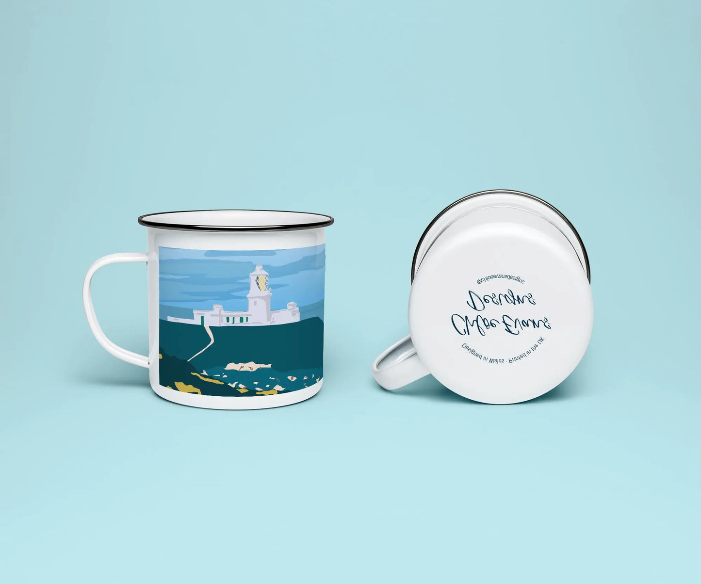 A mockup of a white enamel mug from two perspectives, one standing upright showing the print of Strumble Head lighthouse, and the other of it on its side showing the branded base stamp on the bottom; on a light blue background.