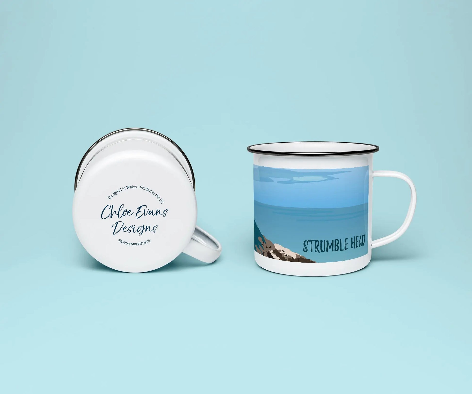 A mockup of a white enamel mug from two perspectives, one standing upright showing the print of Strumble Head lighthouse, and the other of it on its side showing the branded base stamp on the bottom; on a light blue background.