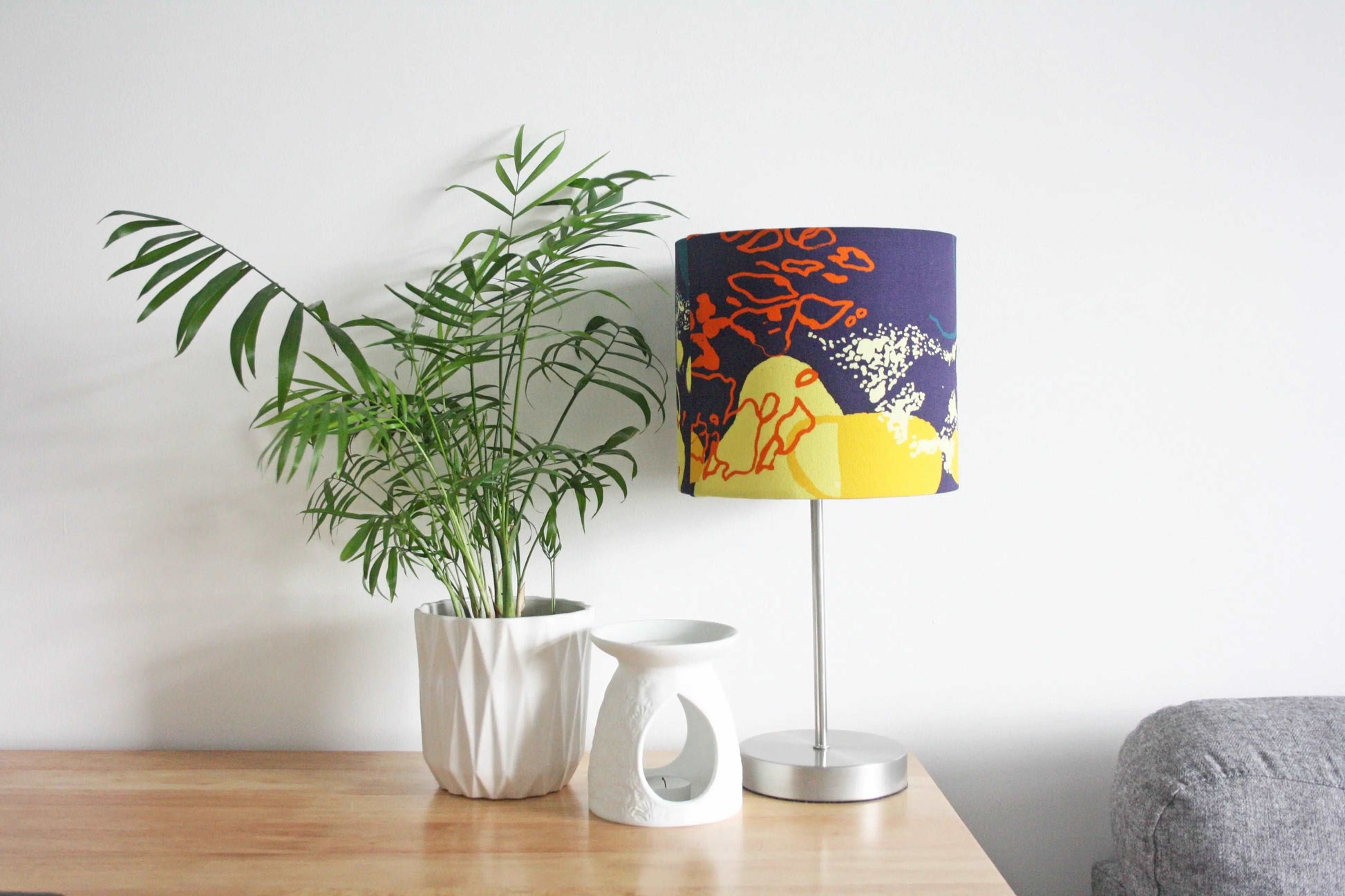 Photo of 20cm navy, yellow and orange abstract print handmade lampshade on silver table lamp with plant and wax melt burner