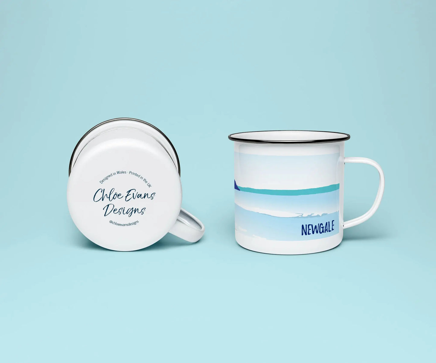 A white enamel mug from two perspectives: one of the mug on its side showing the branded base stamp on the bottom of the mug, and the other of the mug upright showing the blue print of Newgale beach; all on a light blue background.