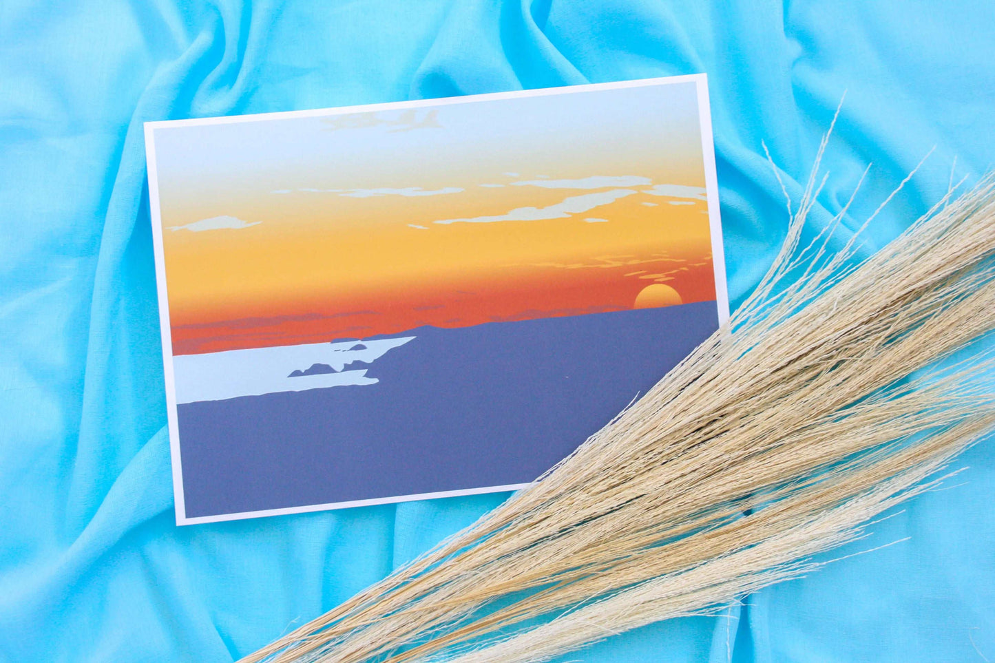 Photo of red, blue and yellow Newgale sunset print on blue fabric backdrop with pampas grass prop