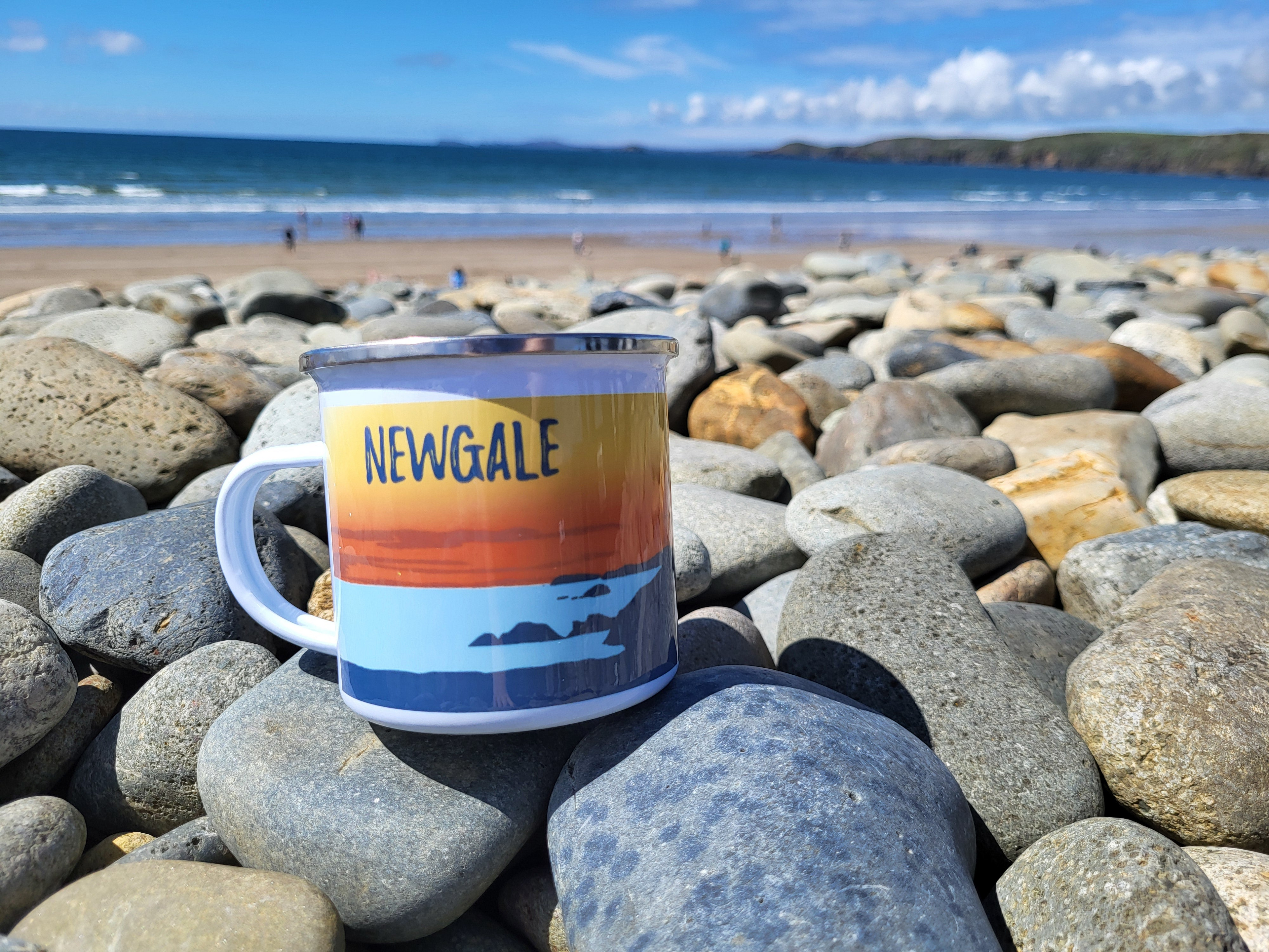 A photo of an enamel mug on rocks at the beach.