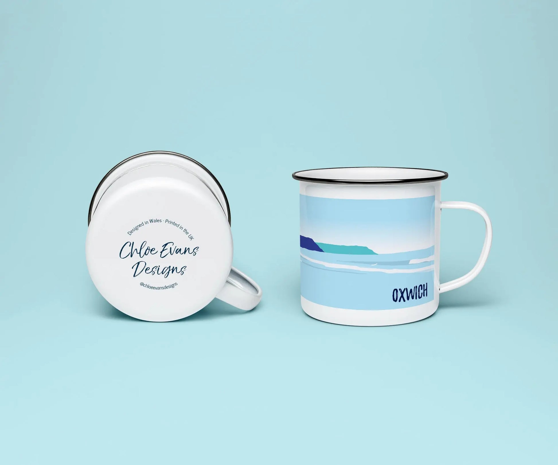 A white enamel mug from two perspectives: one of the mug on its side showing the branded base stamp on the bottom of the mug, and the other of the mug upright showing the blue print of Oxwich beach; all on a light blue background.