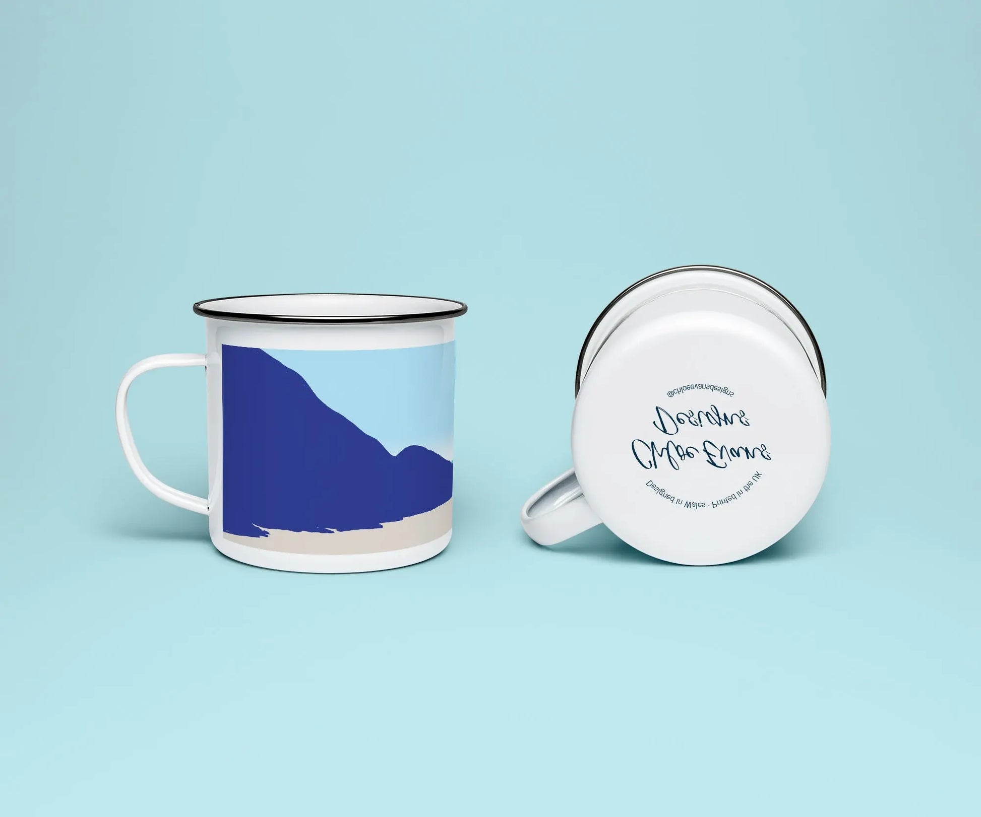 A mock up of a white enamel mug from two perspectives; one of the mug on its side looking at the bottom of the mug and the branded base stamp, and the other of the mug upright showing the print of an orange and blue beach scene, showing the rugged coastline at Penycwm beach, all on a light blue background.