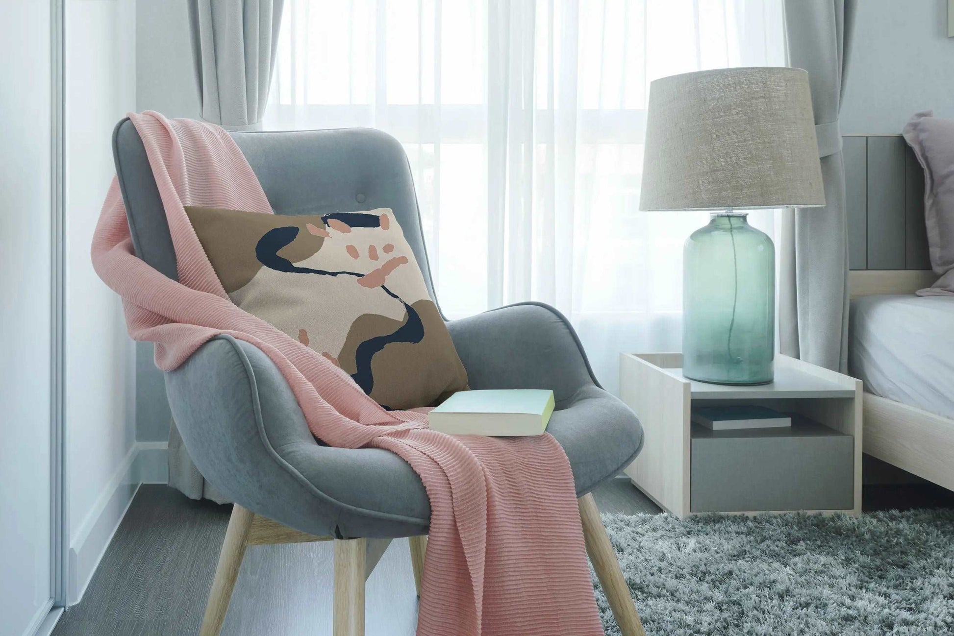 Digital mockup of pink, brown and blue abstract printed cotton handmade cushion on grey armchair with pink blanket in bedroom