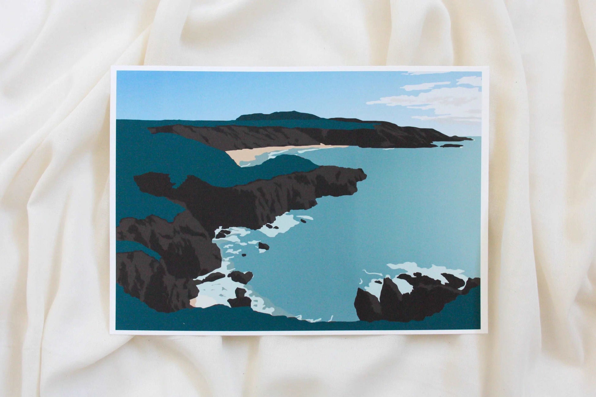 Photo of green, brown and blue Porthor Whistling Sands beach print on cream fabric backdrop