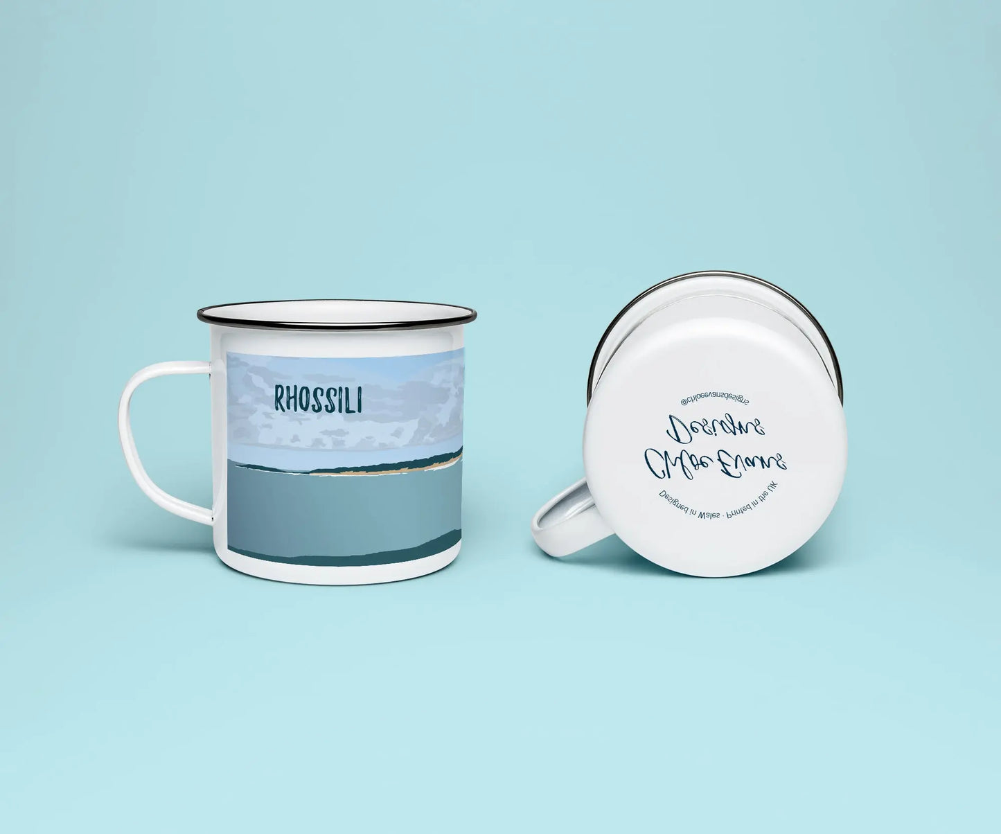 A white enamel mug from two perspectives: one of the mug on its side showing the branded base stamp on the bottom of the mug, and the other of the mug upright showing the green and blue print of Rhossili beach; all on a light blue background.