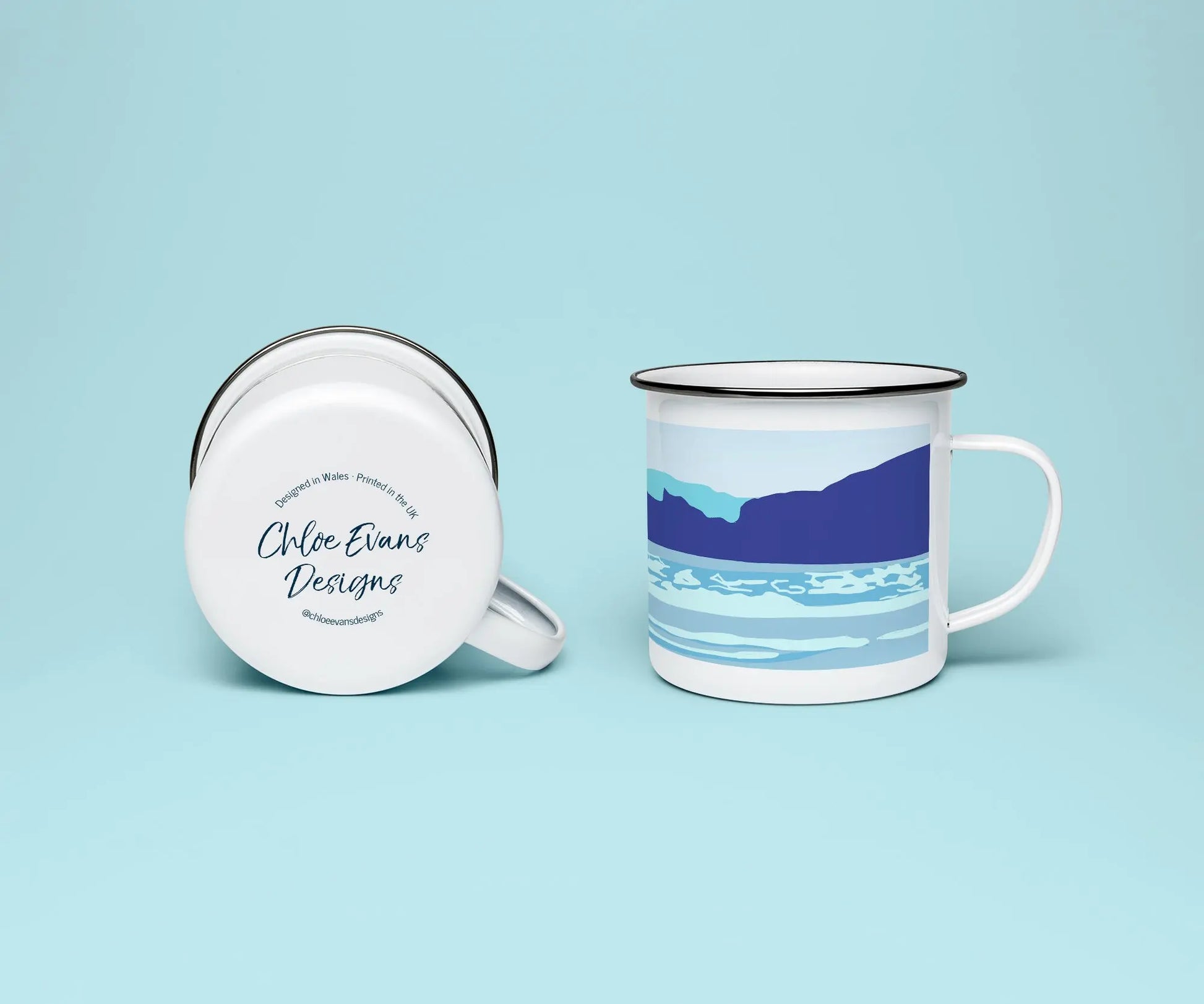 A white enamel mug from two perspectives: one of the mug on its side showing the branded base stamp on the bottom of the mug, and the other of the mug upright showing the blue print of ocean waves and cliffs; all on a light blue background.