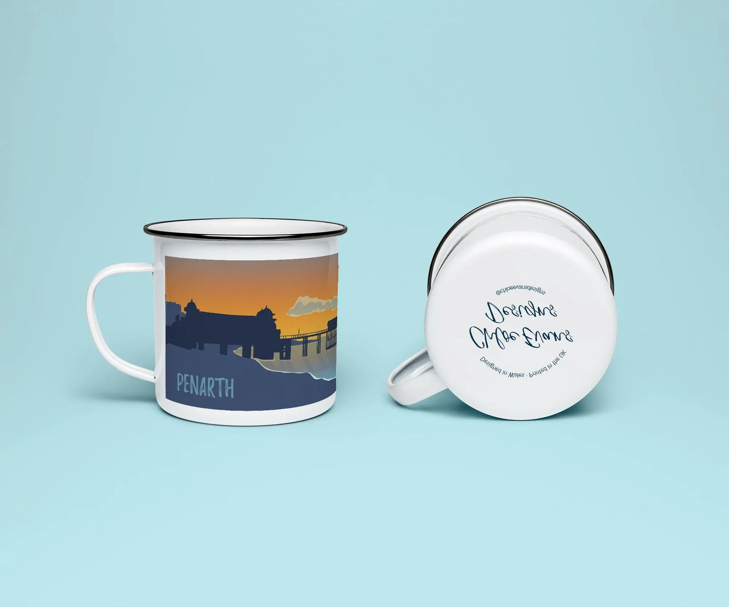 A white enamel mug from two perspectives: one of the mug on its side showing the branded base stamp on the bottom of the mug, and the other of the mug upright showing Penarth pier at sunrise; all on a light blue background.