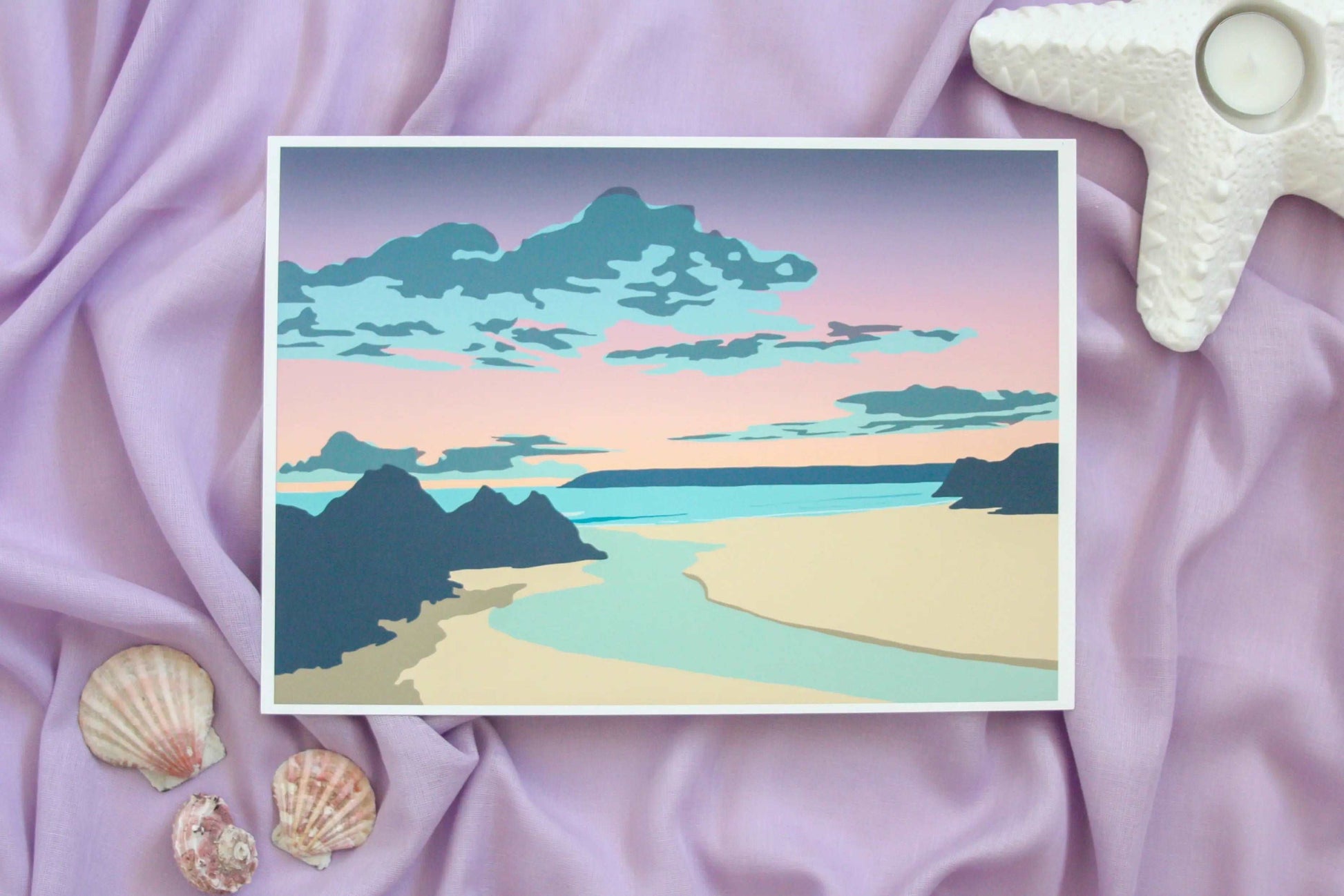 Photo of Three cliffs bay sunset print on purple fabric backdrop with starfish tealight holder and shells