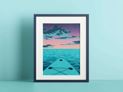 A mockup of an illustration in a frame. The illustration is of a purple and pink sunset over the blue ocean, with the end of a blue paddleboard visible on the foreground. The frame is shown against a light blue background.