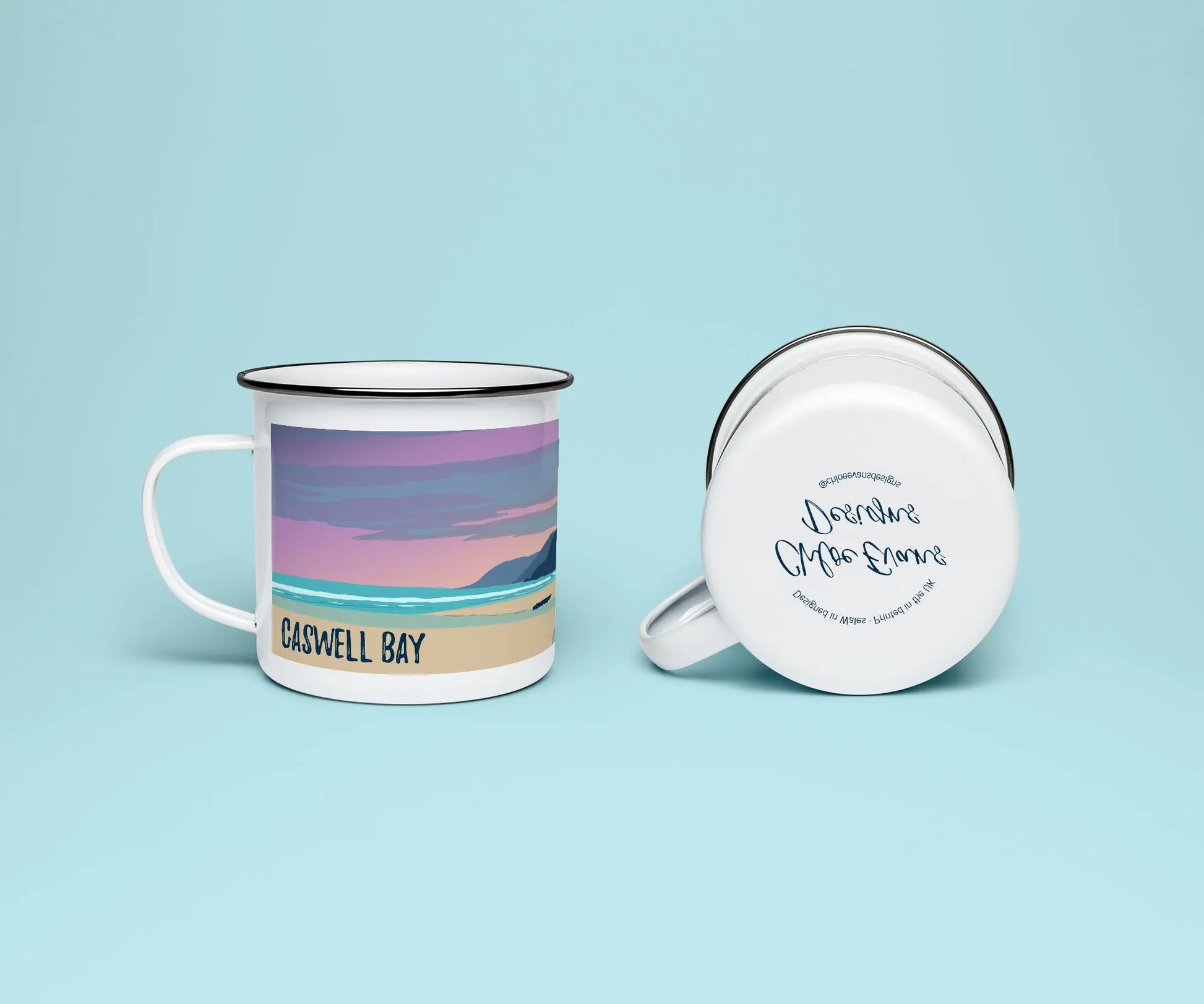 A white enamel mug from two perspectives: one of the mug on its side showing the branded base stamp on the bottom of the mug, and the other of the mug upright showing the pink, orange and blue print of Caswell beach at sunset; all on a light blue background.