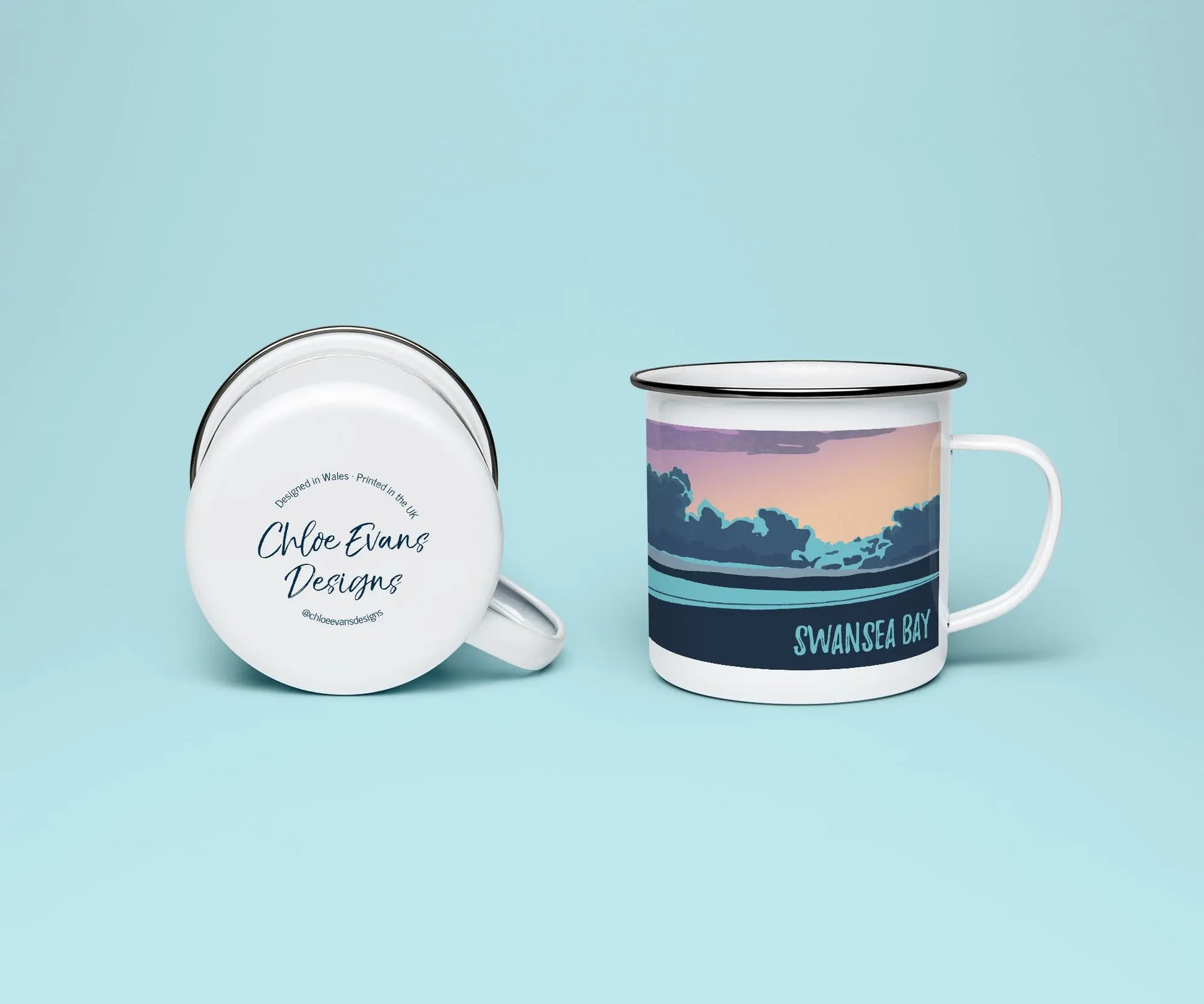 A mock up of a white enamel mug from two perspectives; one of the mug on its side looking at the bottom of the mug and the branded base stamp, and the other of the mug upright showing the print of an purple, orange, and blue beach scene, showing Swansea bay at sunset, all on a light blue background.