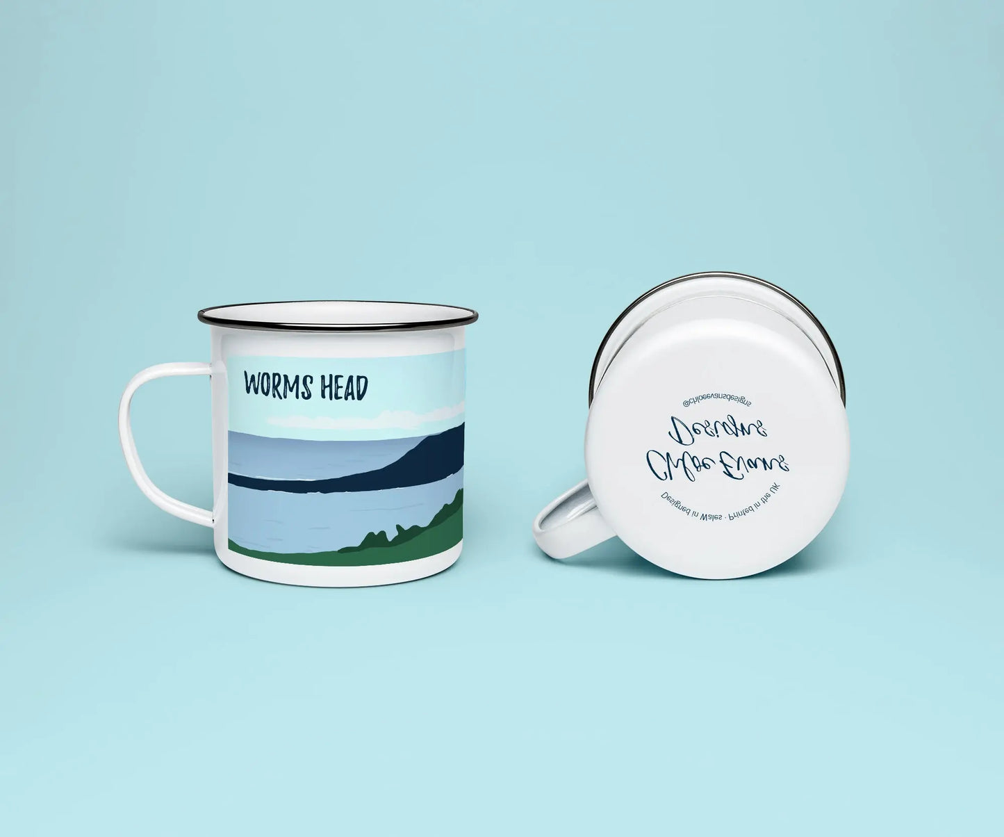 A mock up of a white enamel mug from two perspectives; one of the mug on its side looking at the bottom of the mug and the branded base stamp, and the other of the mug upright showing the print of an green and blue beach scene, showing Worm's Head at Rhossili, all on a light blue background.