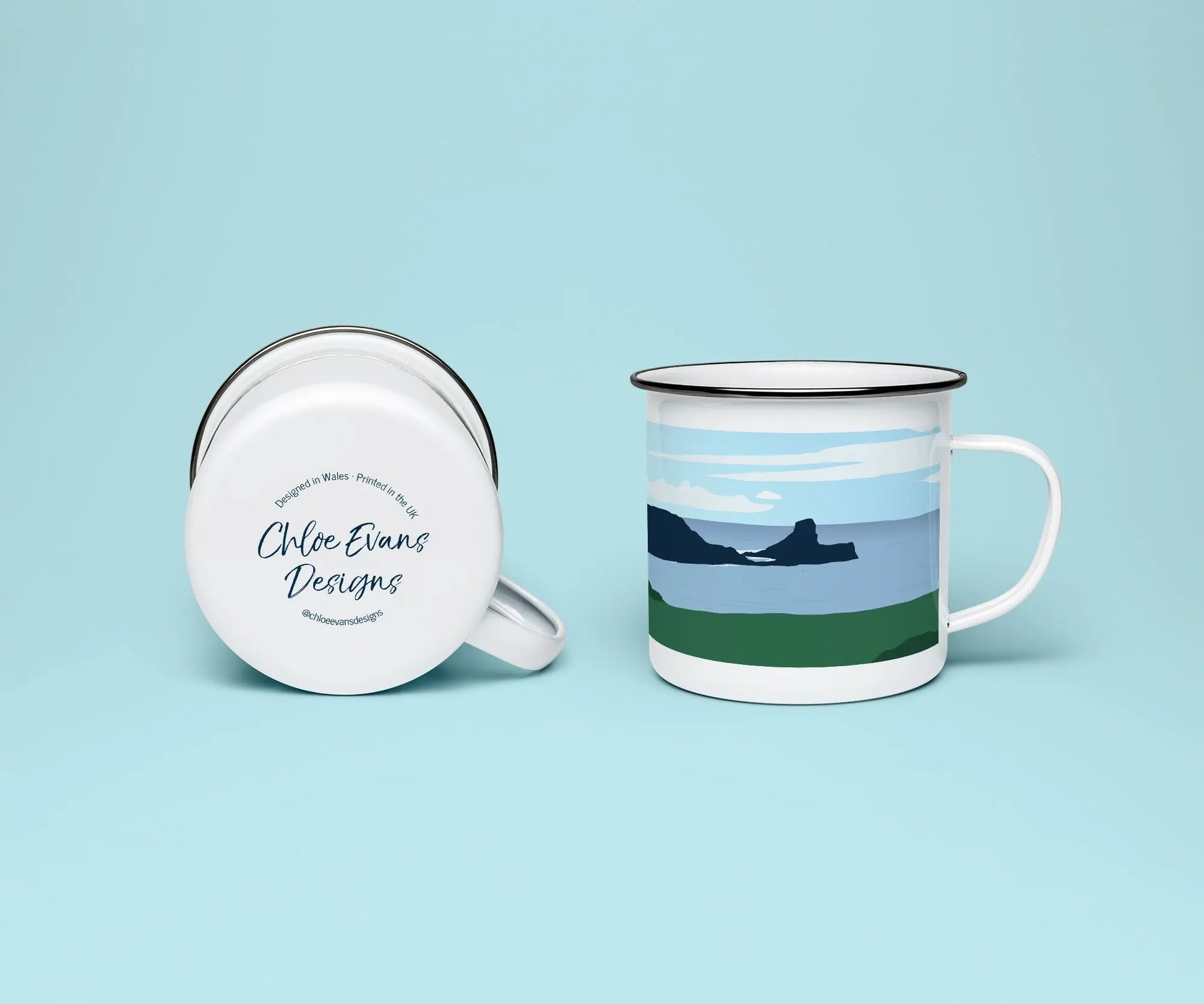 A mock up of a white enamel mug from two perspectives; one of the mug on its side looking at the bottom of the mug and the branded base stamp, and the other of the mug upright showing the print of an green and blue beach scene, showing Worm's Head at Rhossili, all on a light blue background.